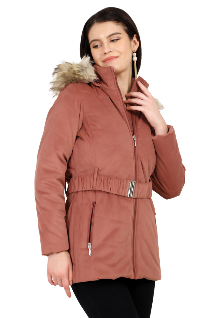 A side profile of a woman standing highlights Coatsnmore’s onion pink velvet quilted jacket, featuring a mandarin collar, removable hood, adjustable waistband zip closure, concealed zippered side pockets and blue jeans with her left hand on the collar.